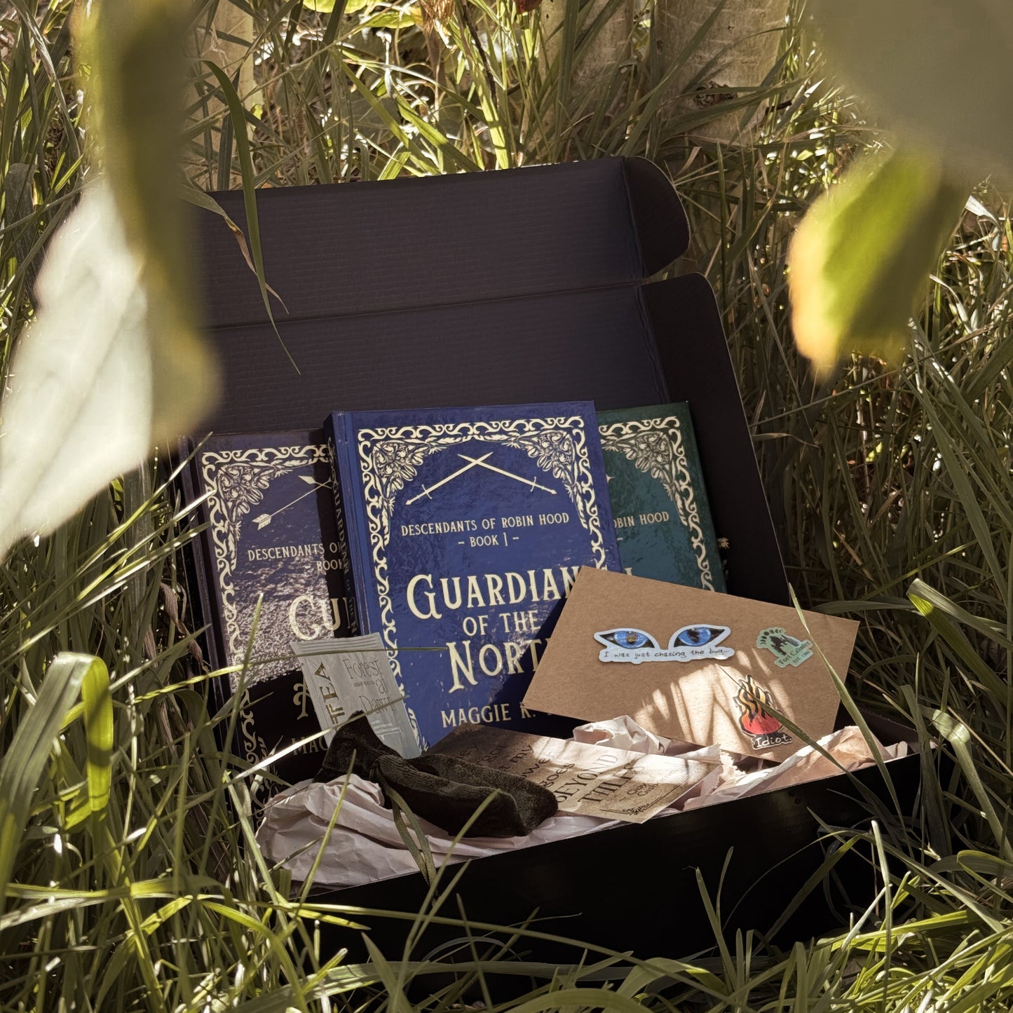 Box with hardcover books and other items in a grassy forest setting